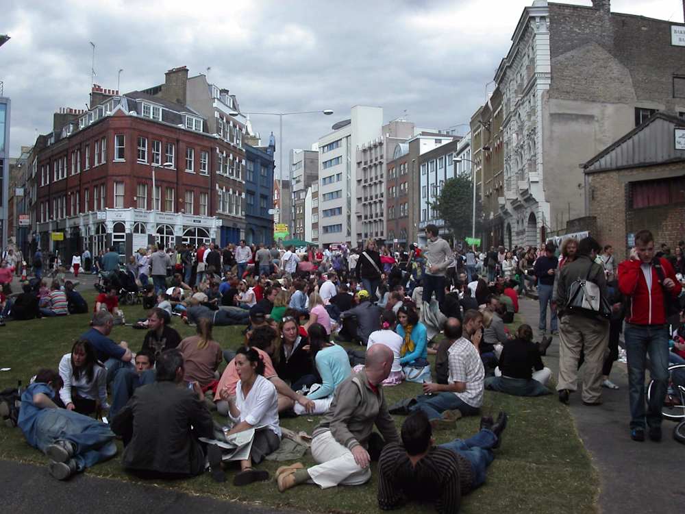 A large group of people sitting and lying down on the grass in a city square