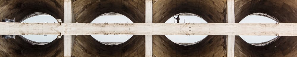 Photograph of the view underneath a concrete bridge, repeated across the image four times and so as to look like the image is reflected.