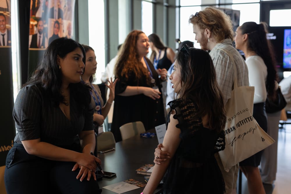 A student speaks to an employer across a table filled with brand merchandise.
