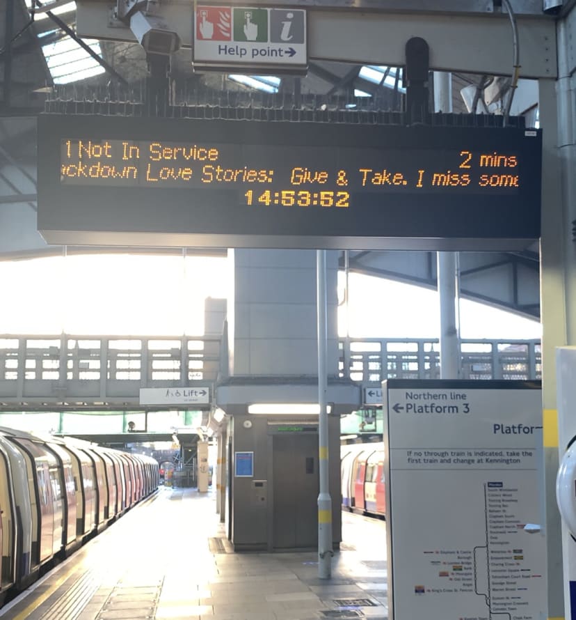 Photo of platform sign at a train station, reading: ''ckdown Love Stories: Give & Take. I miss some