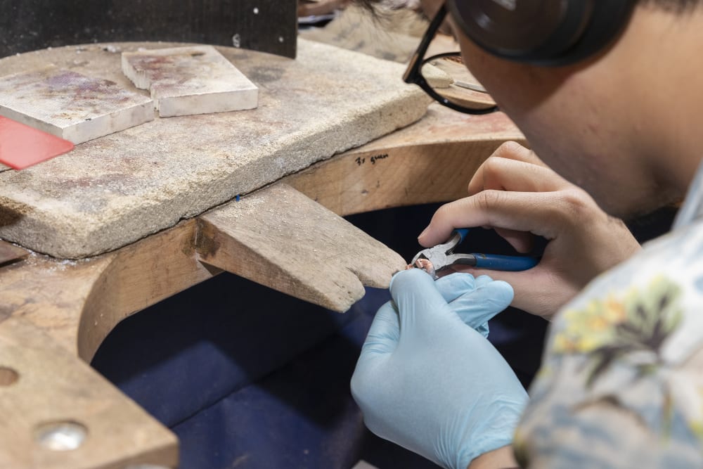 A student at a bench in close-up working with cutters making jewellery. They are wearing blue gloves.