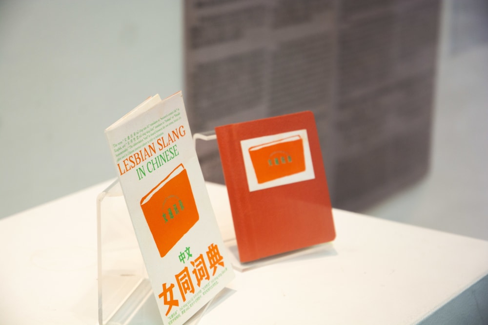 Two red and white books placed on a table in an exhibition behind glass windows.