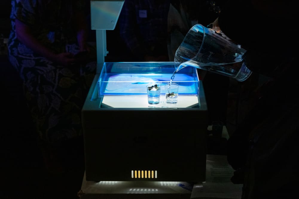 Overhead projector lit blue with a hand pouring liquid into a clear dish