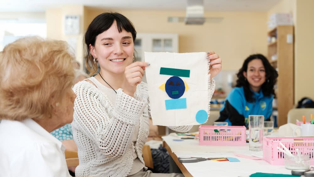 Girl holding up a piece of textile art to show an old lady.