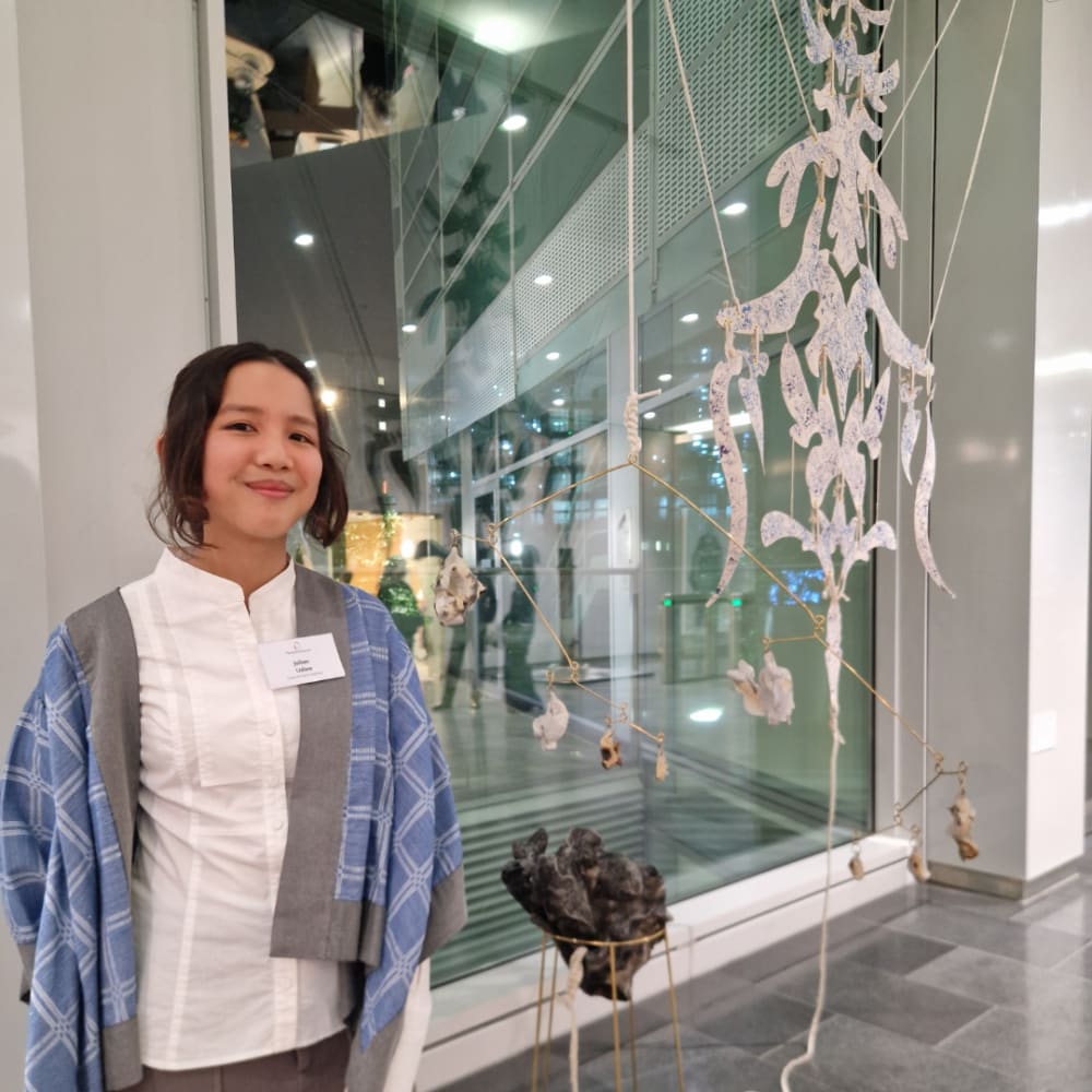 An image of a smiling woman infront of a piece of art