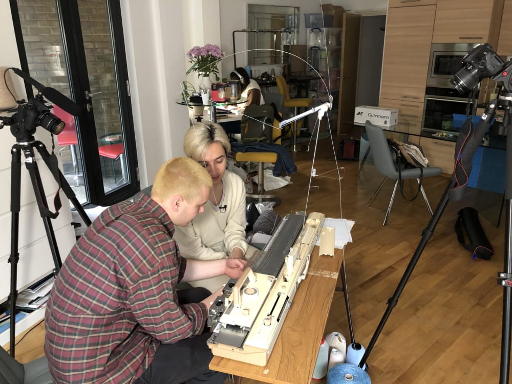Photograph of Elior and Florian looking down at a knitting machine in Florian’s studio. 
