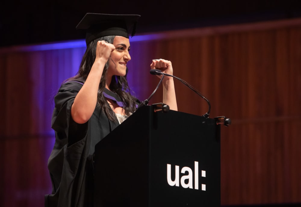 Saadia Kanaan with fists raised in speech at a podium