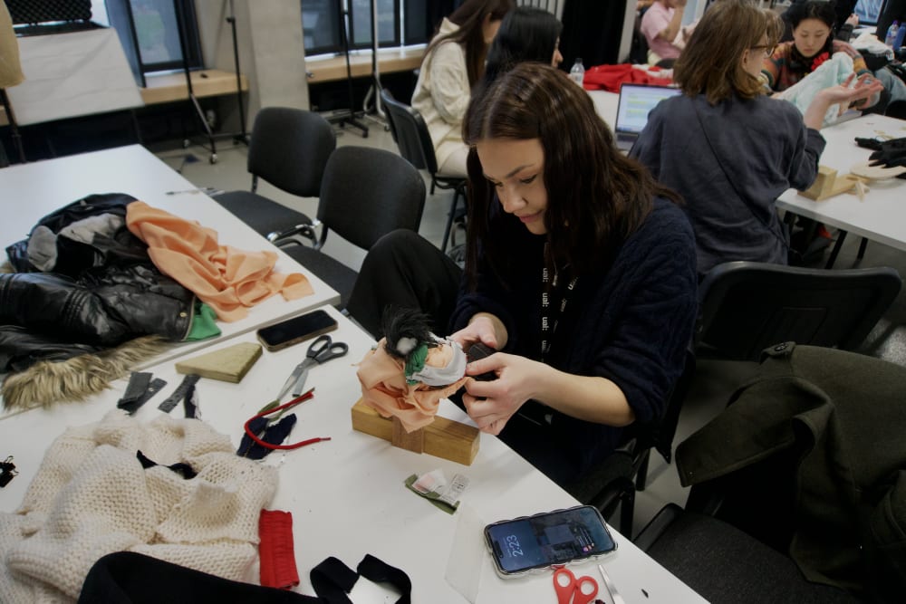 Student sat by a table and crafting an effigy made out of textile and wood.
