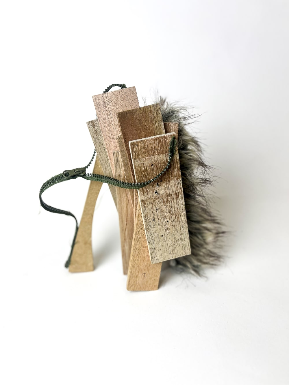 An effigy sculpture made out of wood with a zip and a furry layer against a white background.