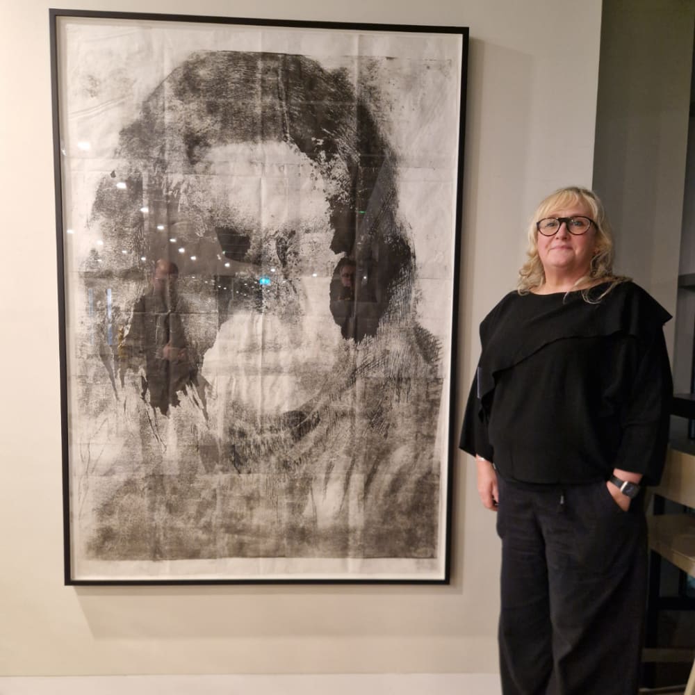 An image of a woman posing in front of a piece of art mounted to a wall