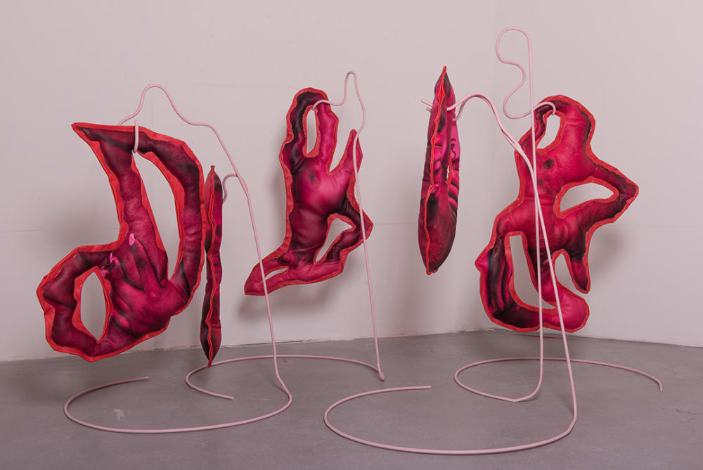 4 standalone sculpture pieces. Pink coloured stuffed material sculptures are supported by pink curved thin metal stands 