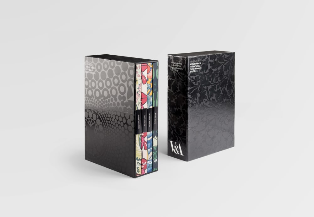 Photo of a book series in a display box. The box has a black and grey circular graphic design on. The 4 books each has a different colour and pattern on the spine.