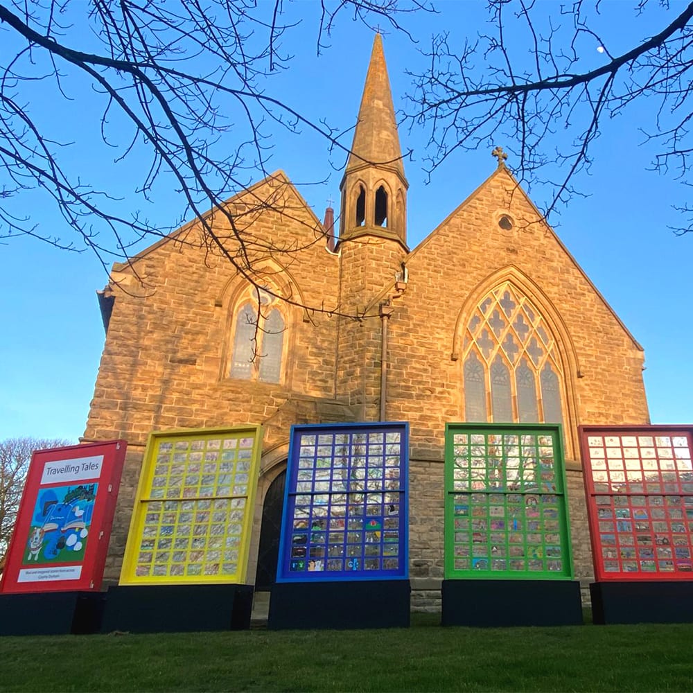 Stone church with steeple behind colourful art display panels under a blue sky