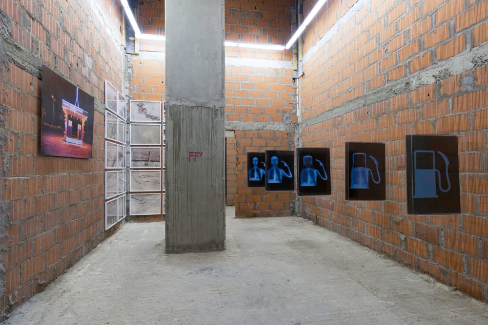 Space with bare brick walls, and light from above. On the walls are photos and negatives.