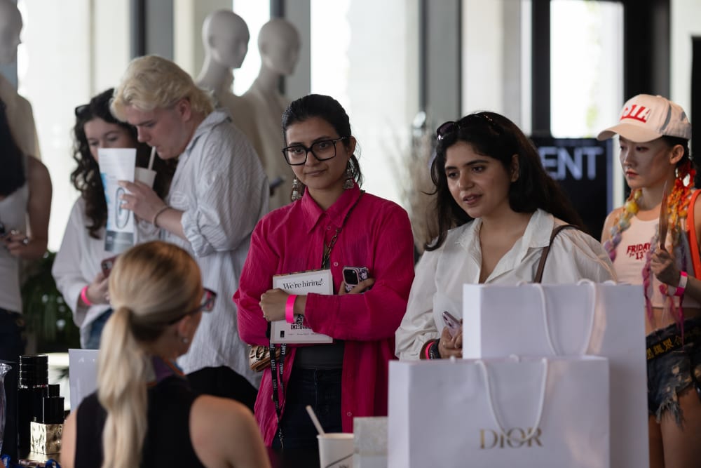 Two students speaks to an employer across a table filled with brand merchandise.