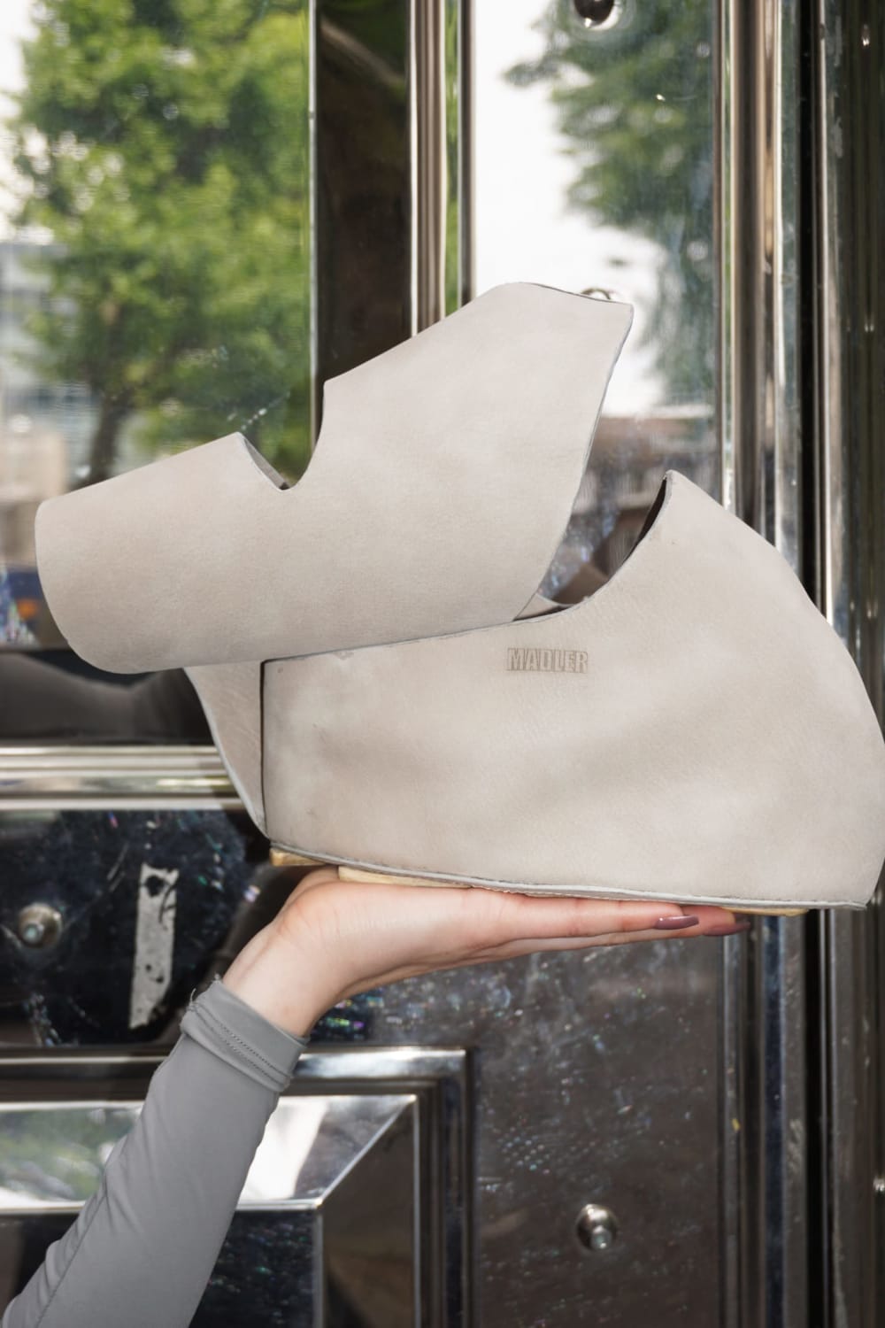 A hand holding a beige bag against a reflective door.