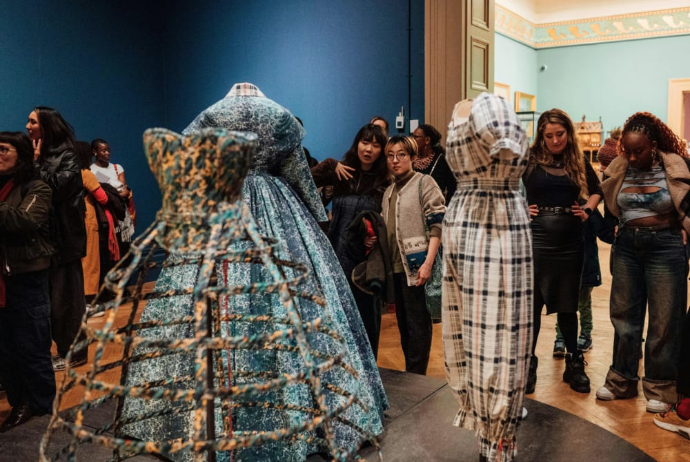 Visitors looking at dresses on mannequins at exhibition.