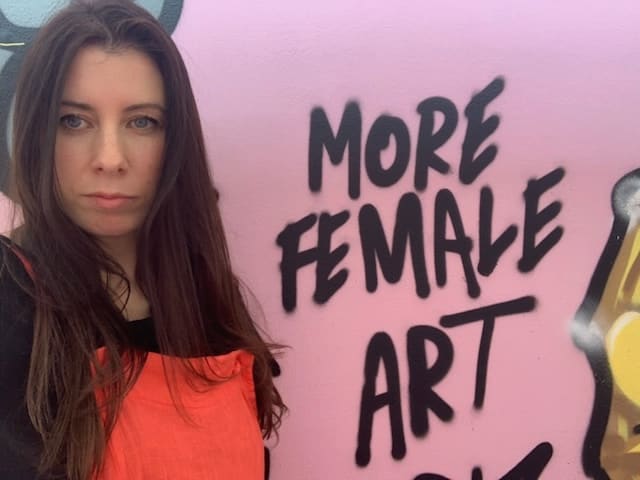 Philippa standing next to some graffiti text that reads 