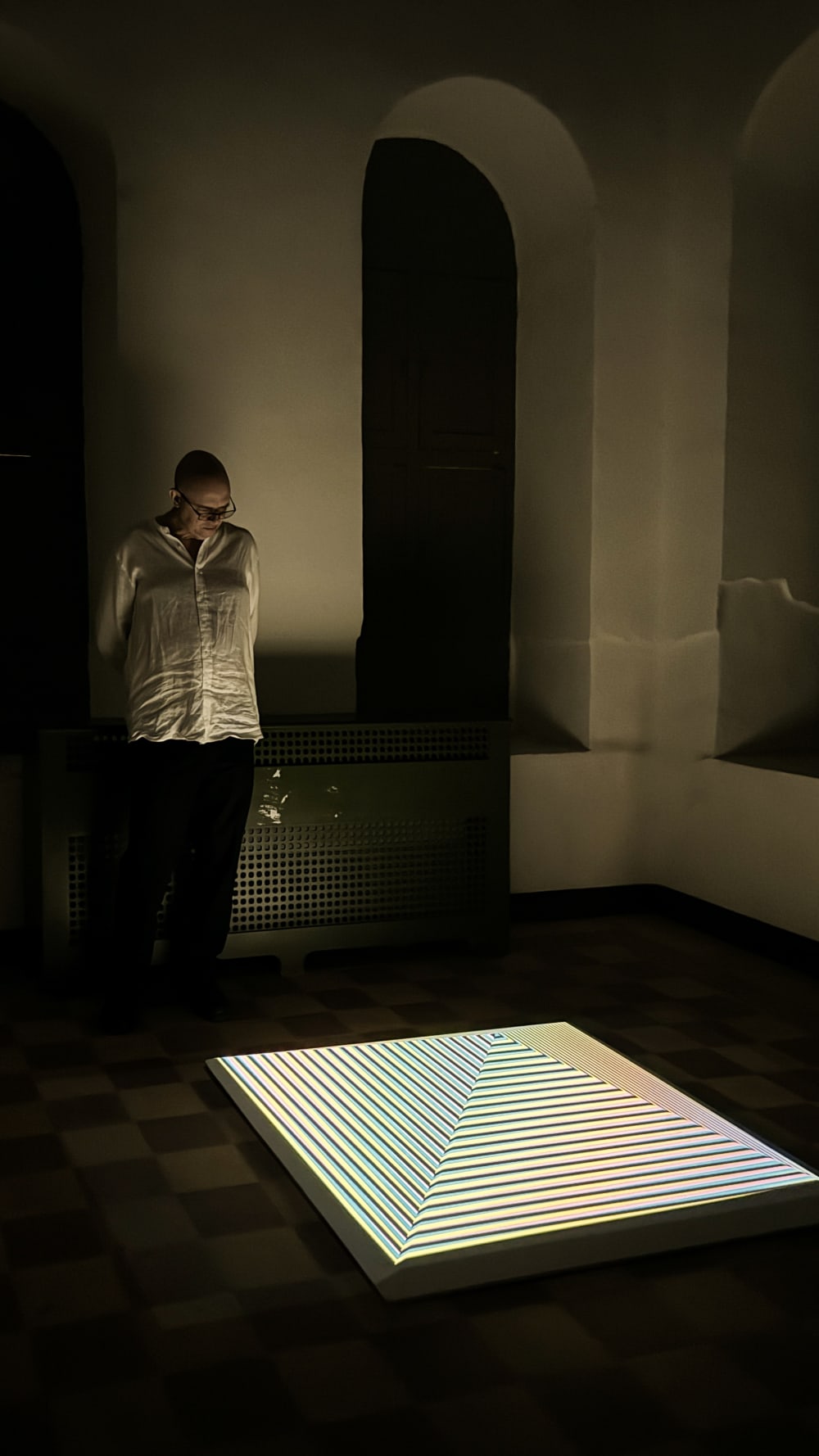A man standing in a dark room, looking down at a lit-up square sculpture.