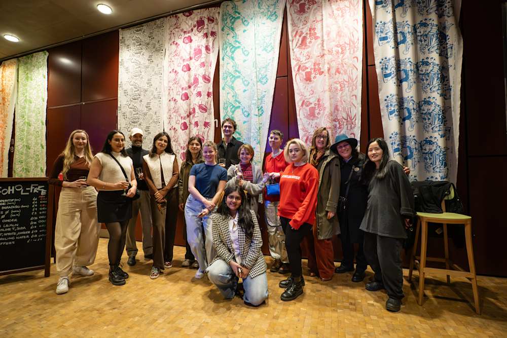 Group of people standing and smiling to the camera. Behind them, large pieces of material hang from the ceiling with different patterns on