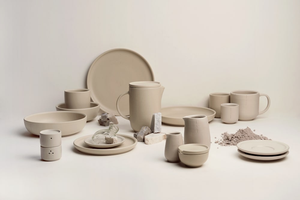 A neatly arranged 14‑piece ceramic tableware set in soft neutral tones, including plates, bowls, and cups with simple circular forms, displayed on a light surface to highlight the minimalist, handcrafted design