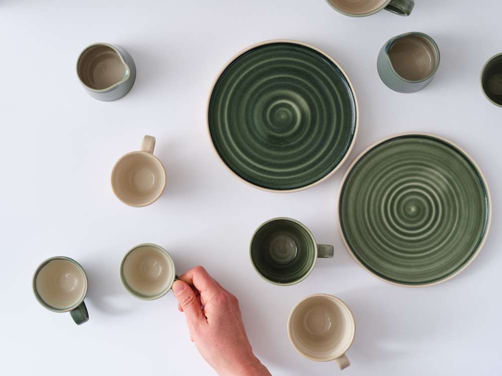Glazed coffee cups and plates with swirl patterns shot from above, with a hand holding one of the cups.