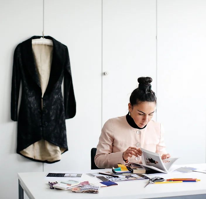 Person sitting at desk looking at magazine, with dress hanging behind. 