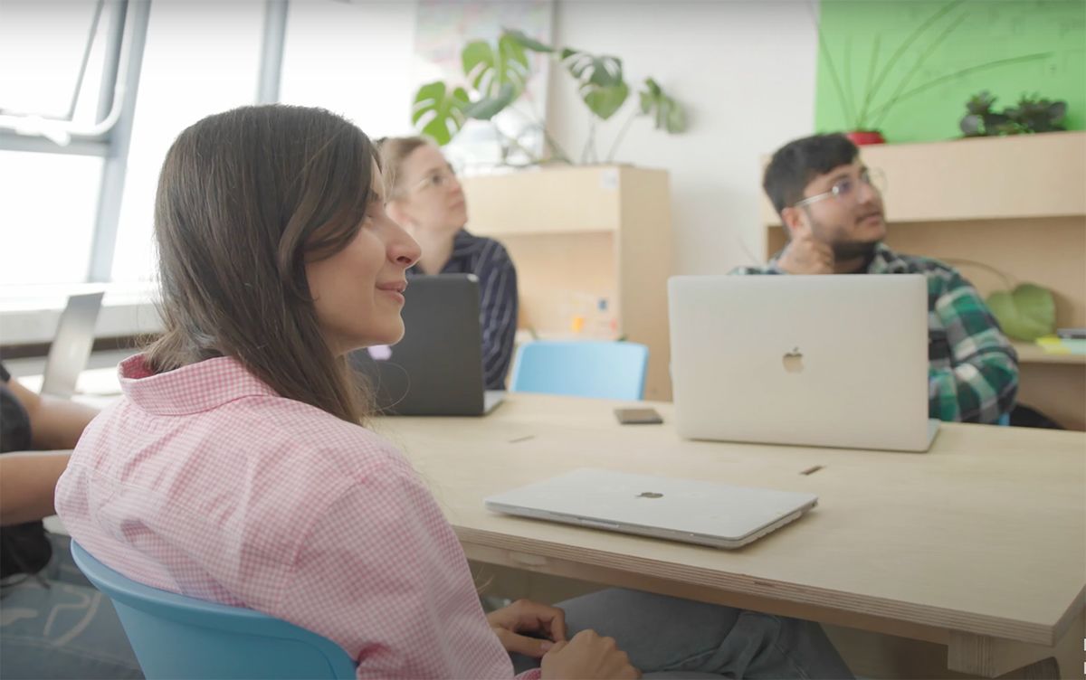 People sit around a table and look off-screen at a presenter.