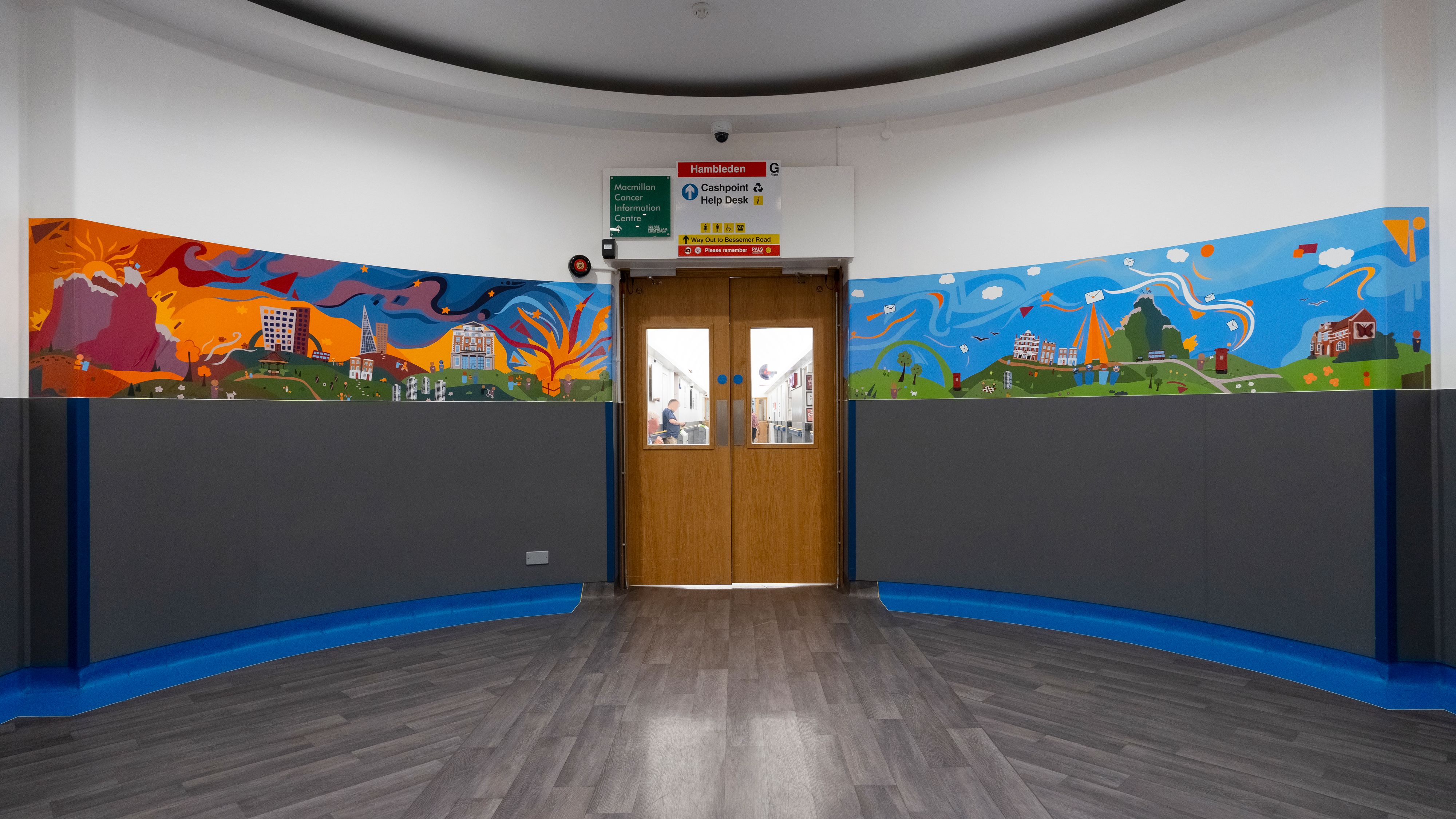 Image shows a set of doors leading to a long corridor with a colourful mural depicting the journey of organ donation on either side of the doors.    