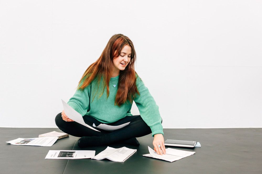 Jaya Twill sits crosslegged in the studio surrounded by notebooks