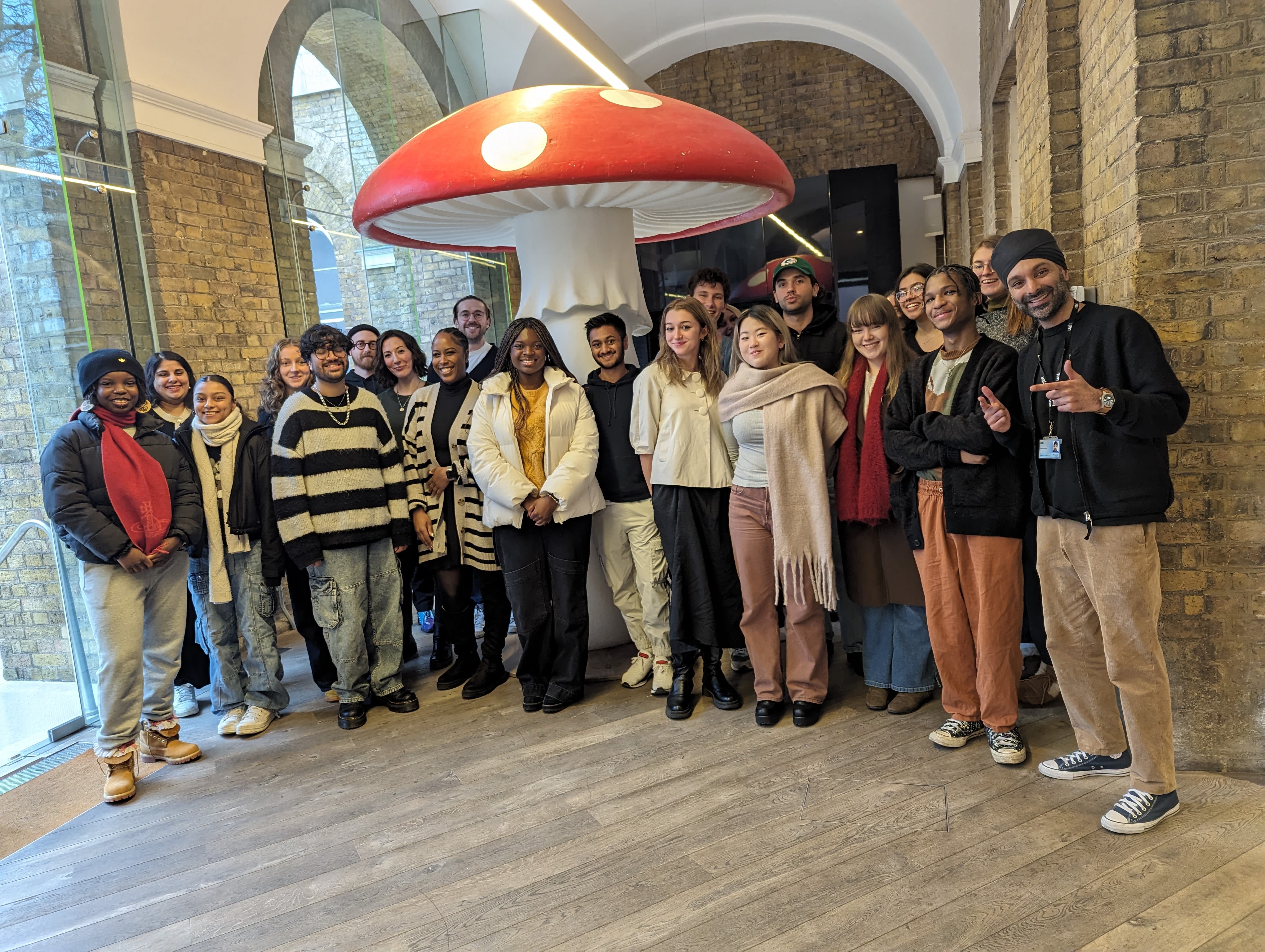 Photograph of a group of students standing infront of a sculpture of a giant red and white mushroom