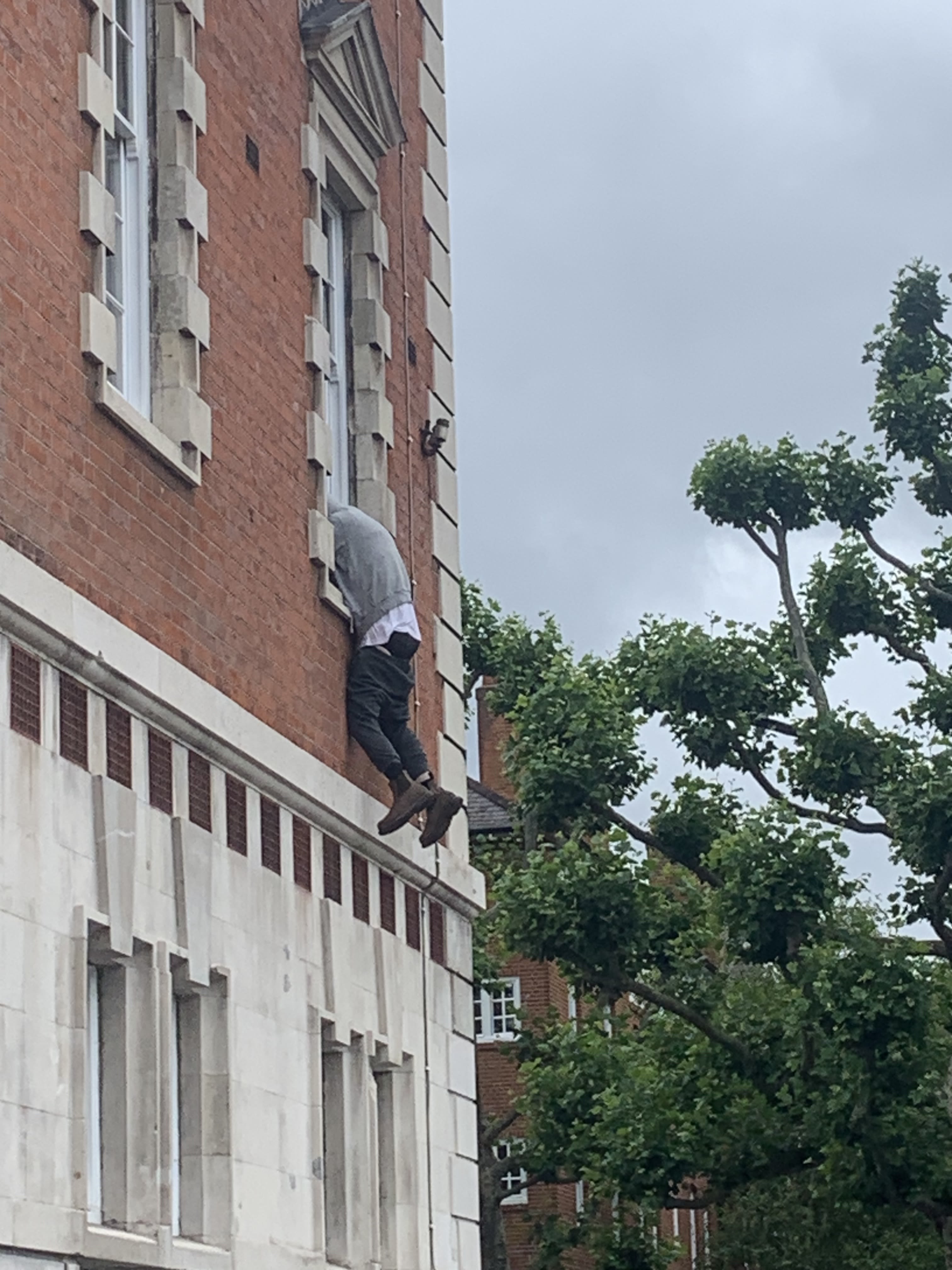 A sculpture of a person hanging out of a second floor window of a building.