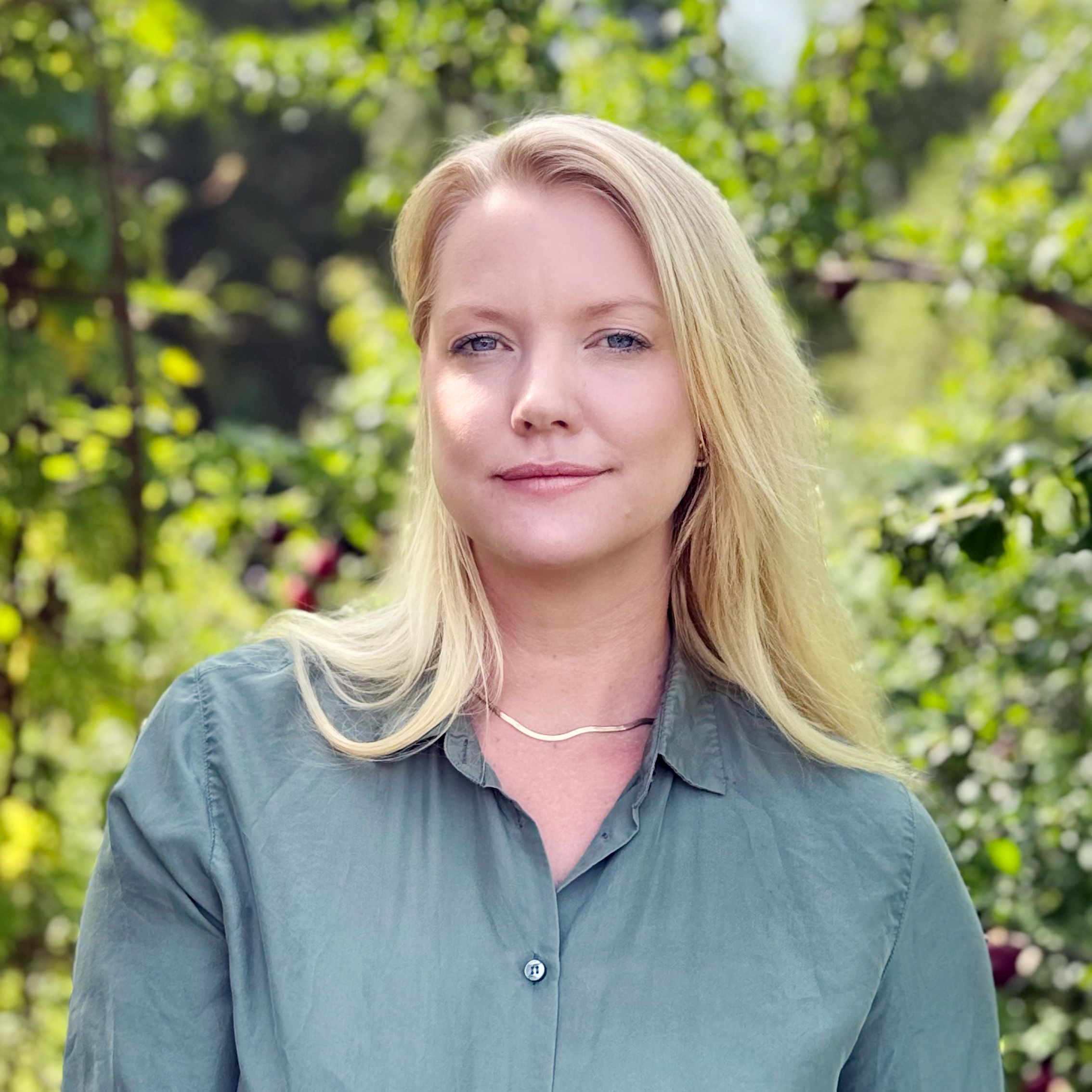 A blonde woman wearing a green blouse with leaves in the background