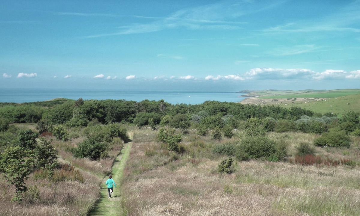 Wide-angle shot of a woman running on a coastal path.