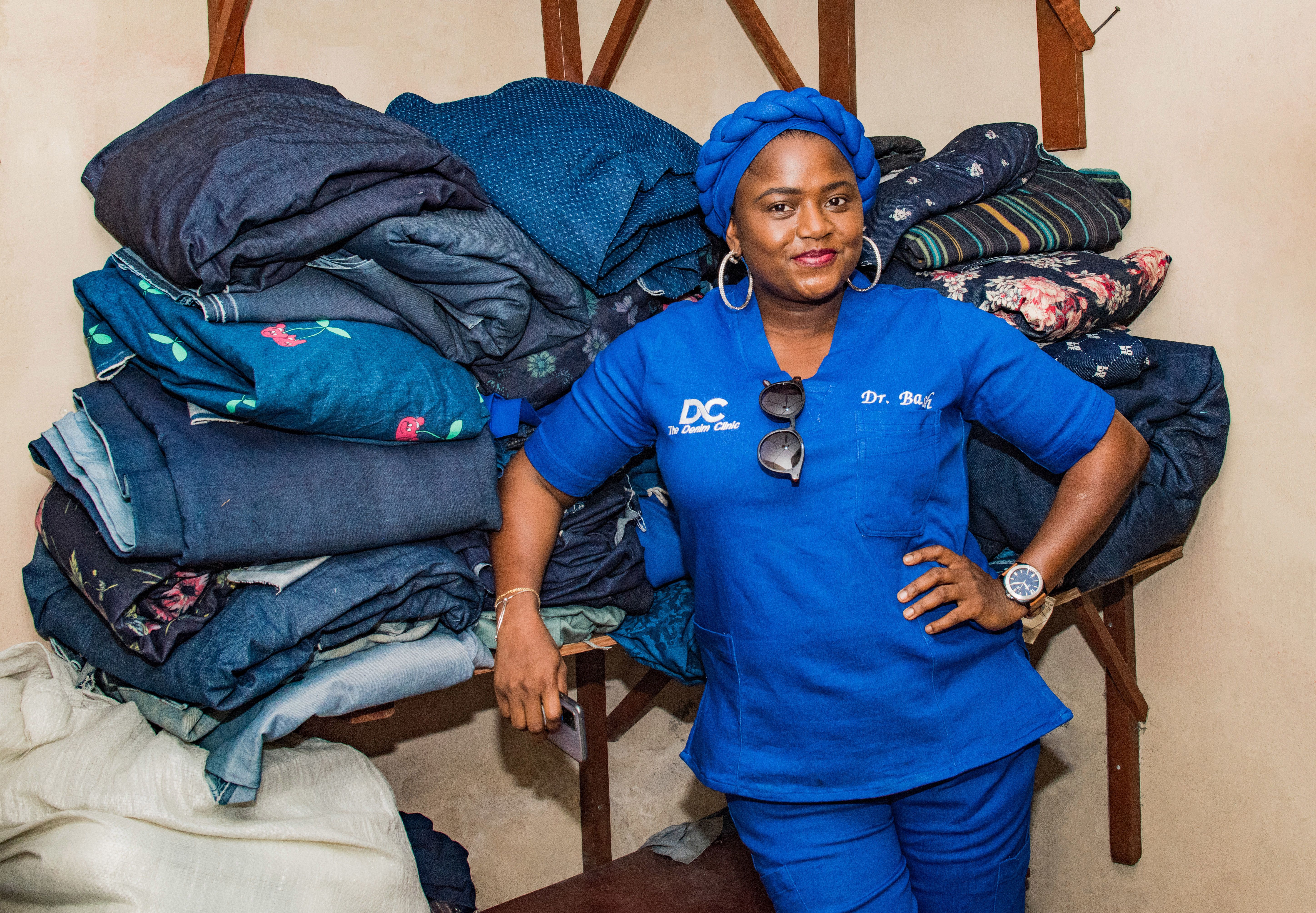 A woman stands in front of a heap of recycled denim garments 