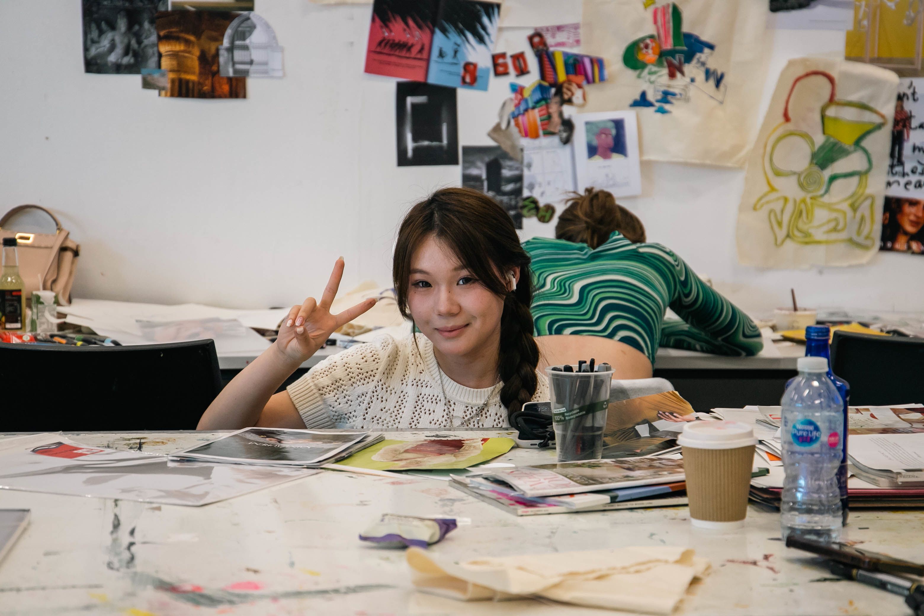 Student smiling and posing for the camera around her desk and craft materials