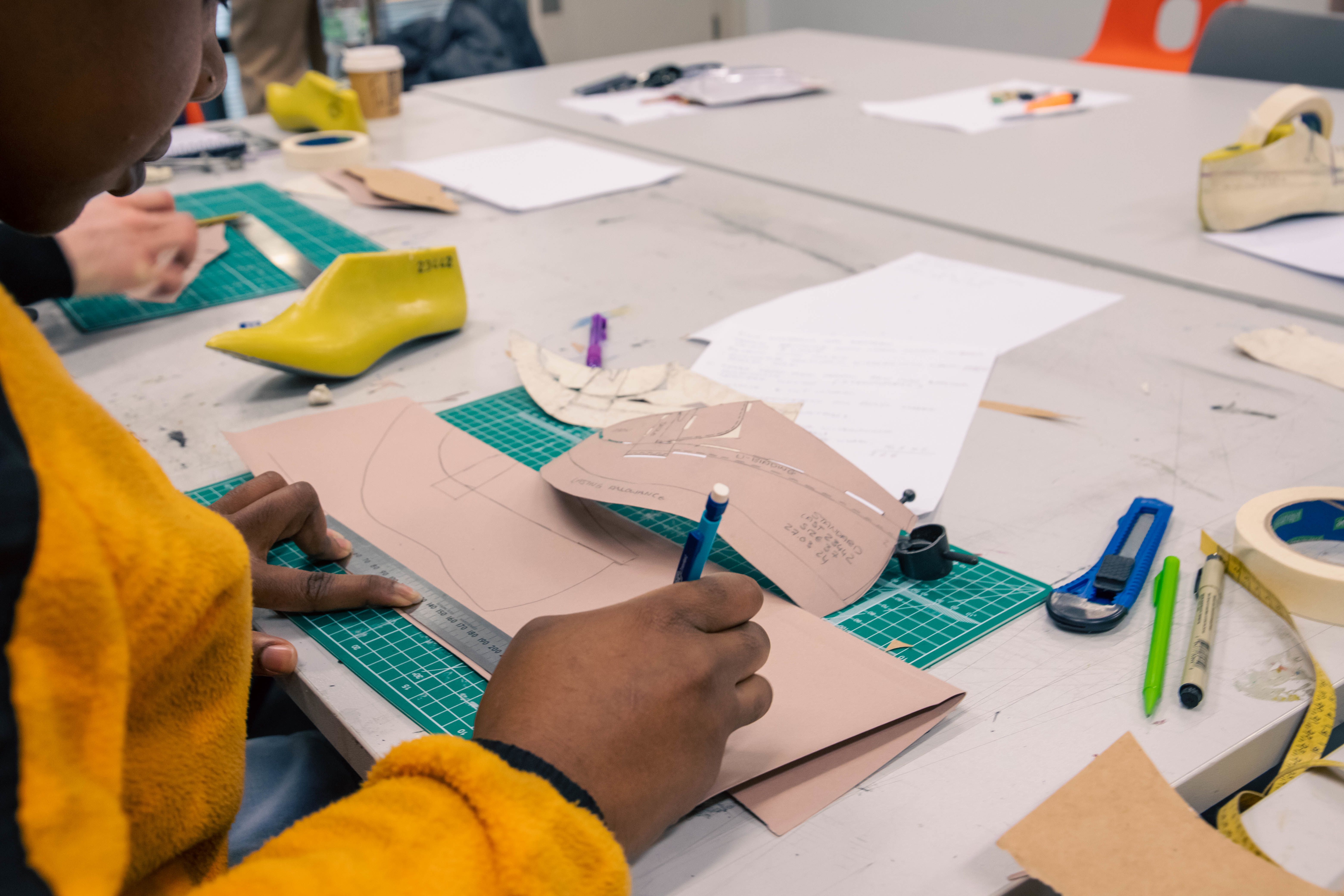 Student working on a shoe pattern, holding a ruler and a pencil