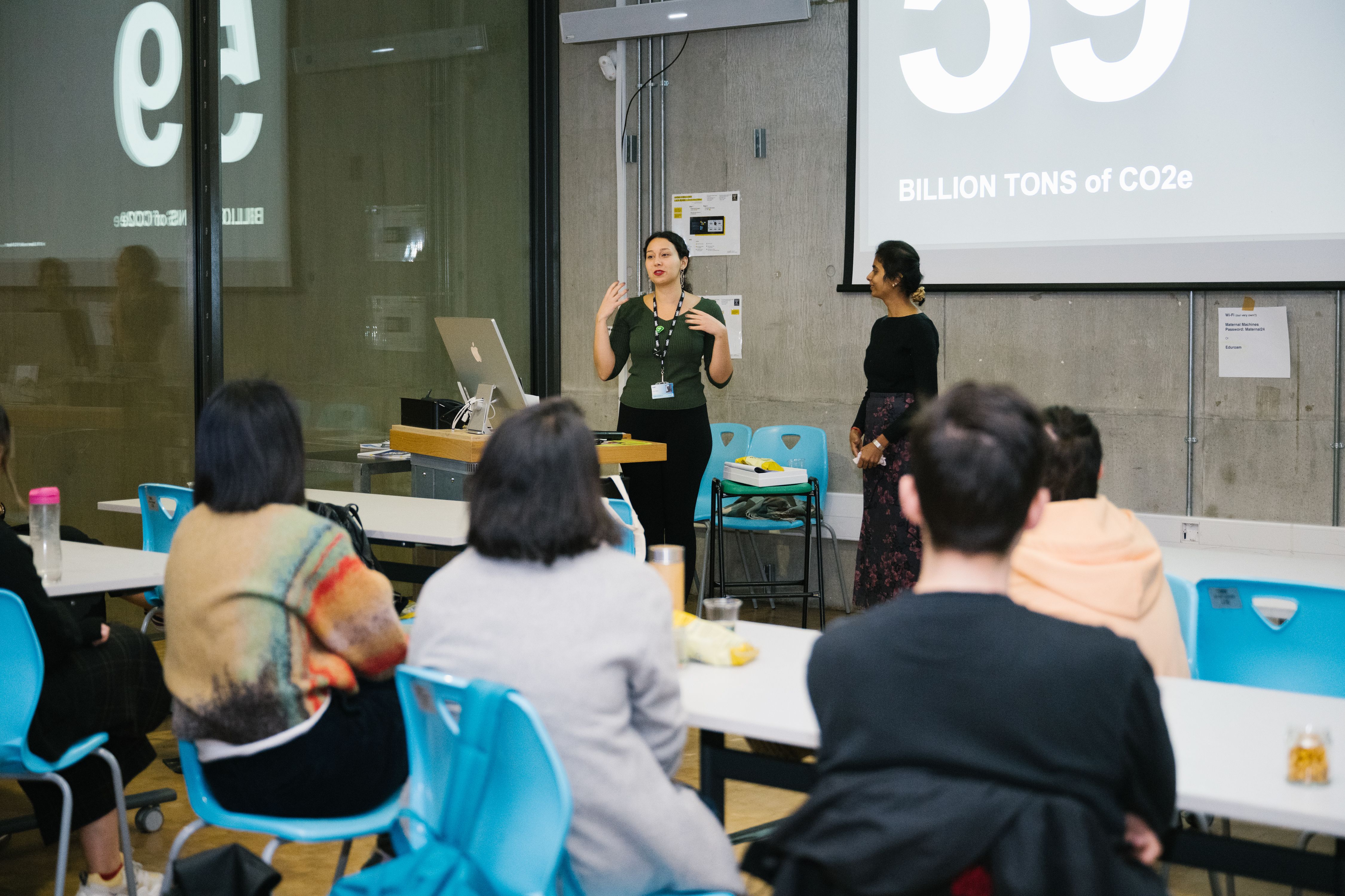 Ozge and Nanthini speaking in front of the workshop. On the screen behind them it says 'Billion tons of CO2e'