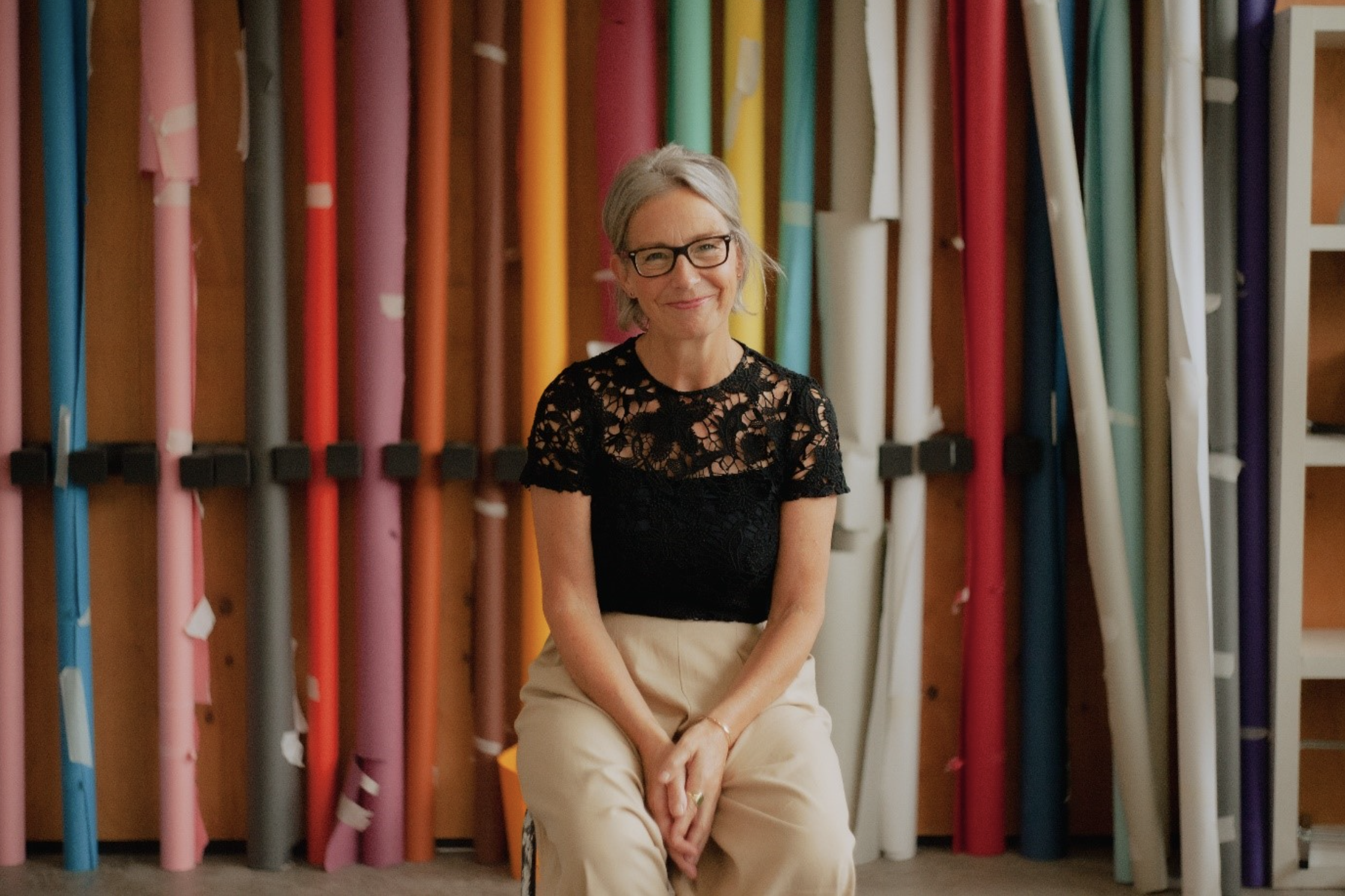 Roni Brown smiling, sitting in front of rolls colourful fabric