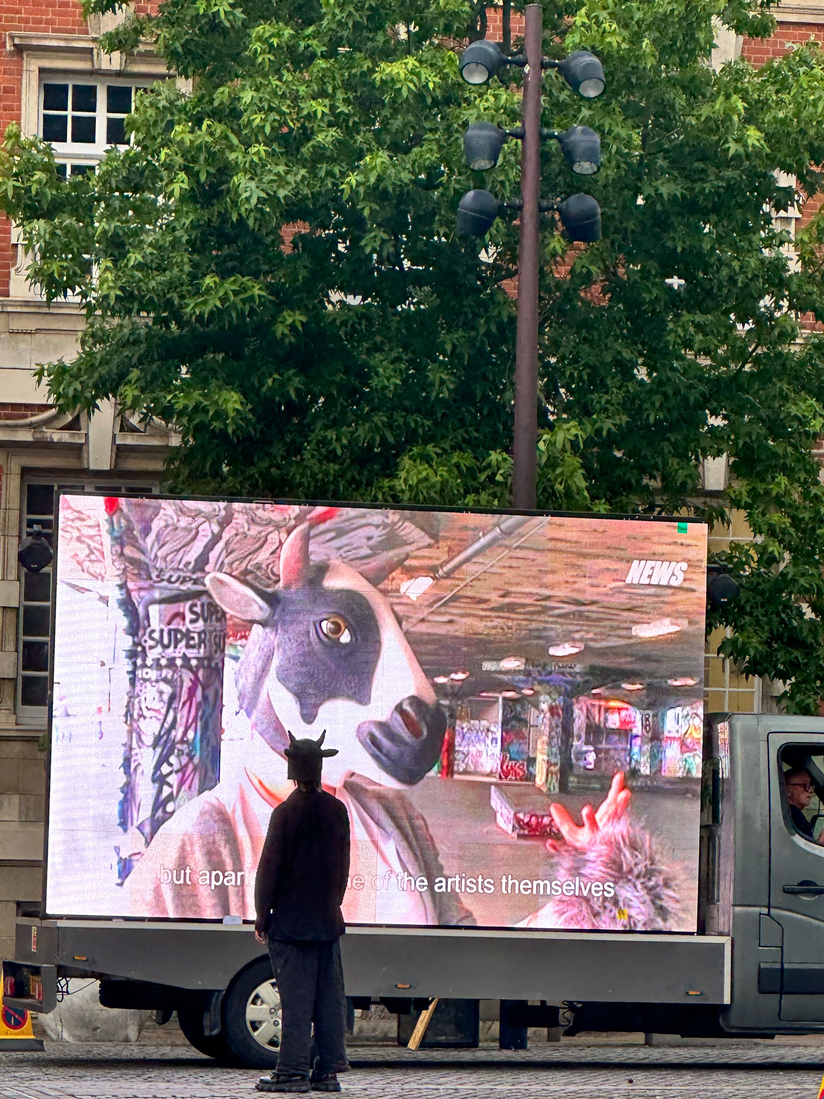 A person wearing a mask standing in front of the film - ‘Everything except a Dog’ by Luo Mengmeng