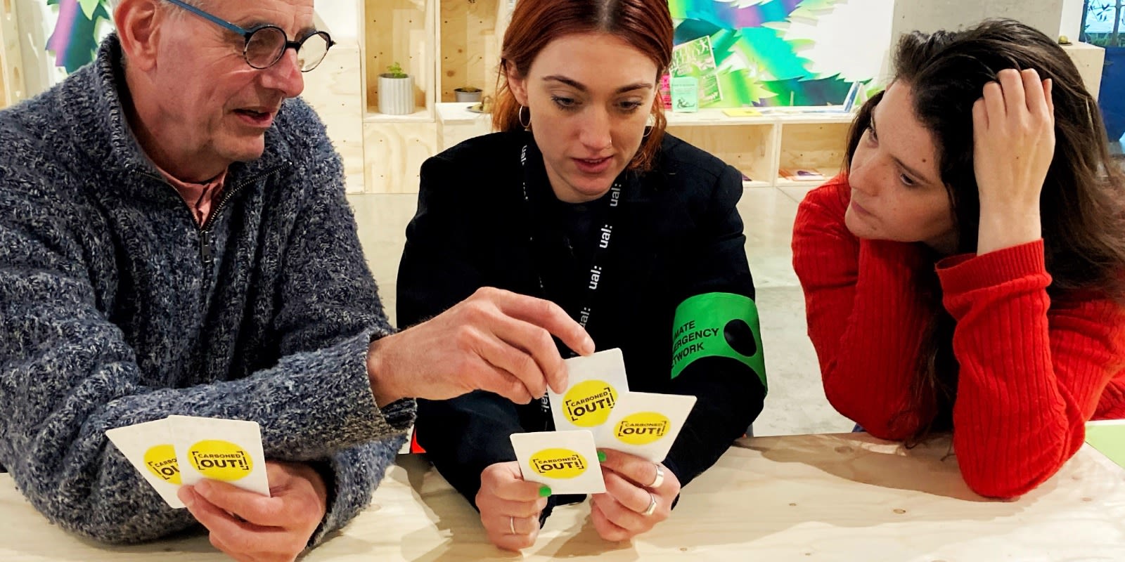 3 people sit around a table playing the board game 'Carboned Out'