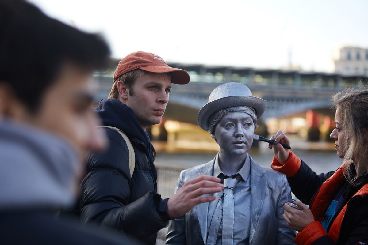 A make-up artist paints the face of an actor playing a living statue.
