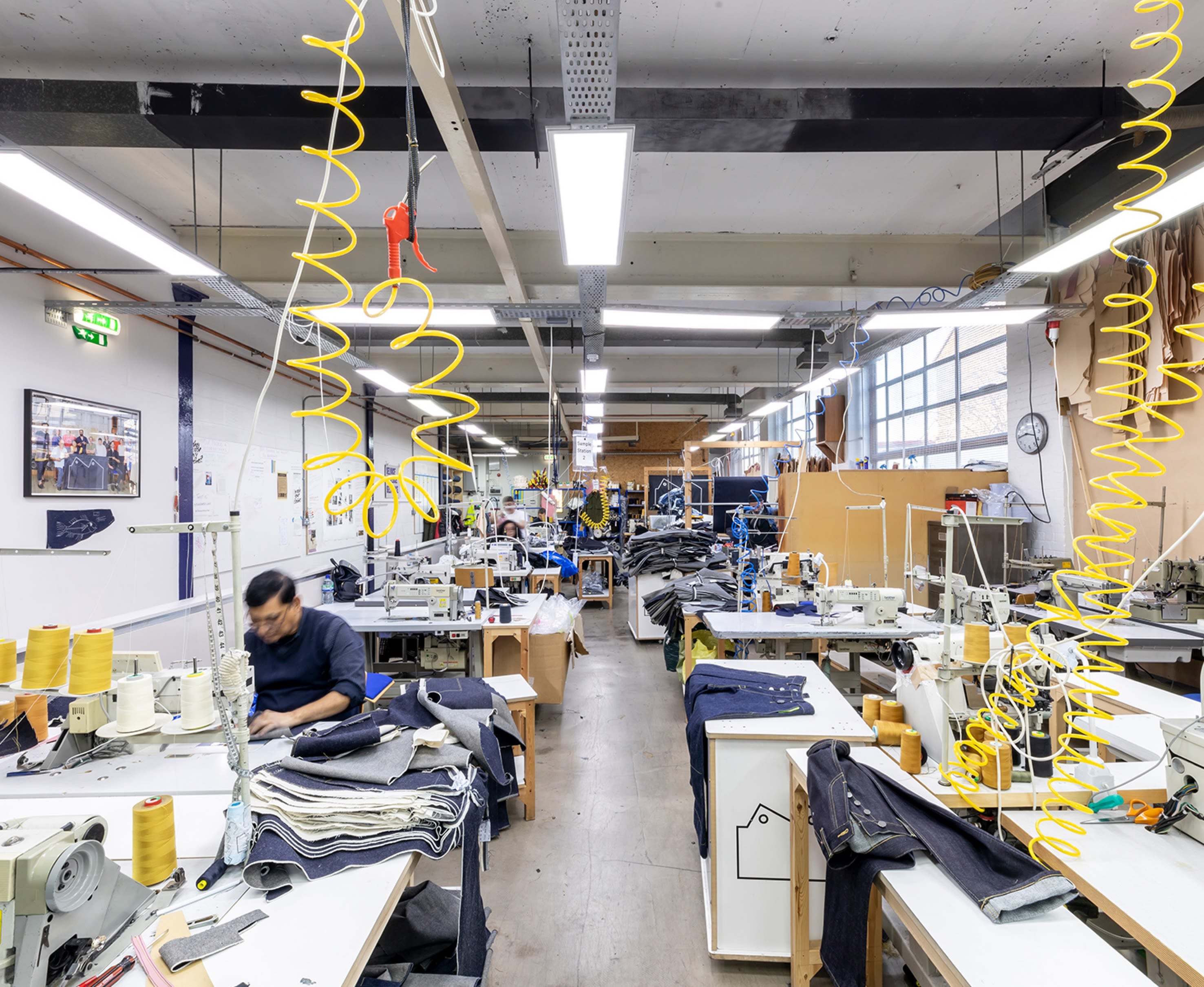A denim production studio with lots of tables and machinery and people working with cuts of denim