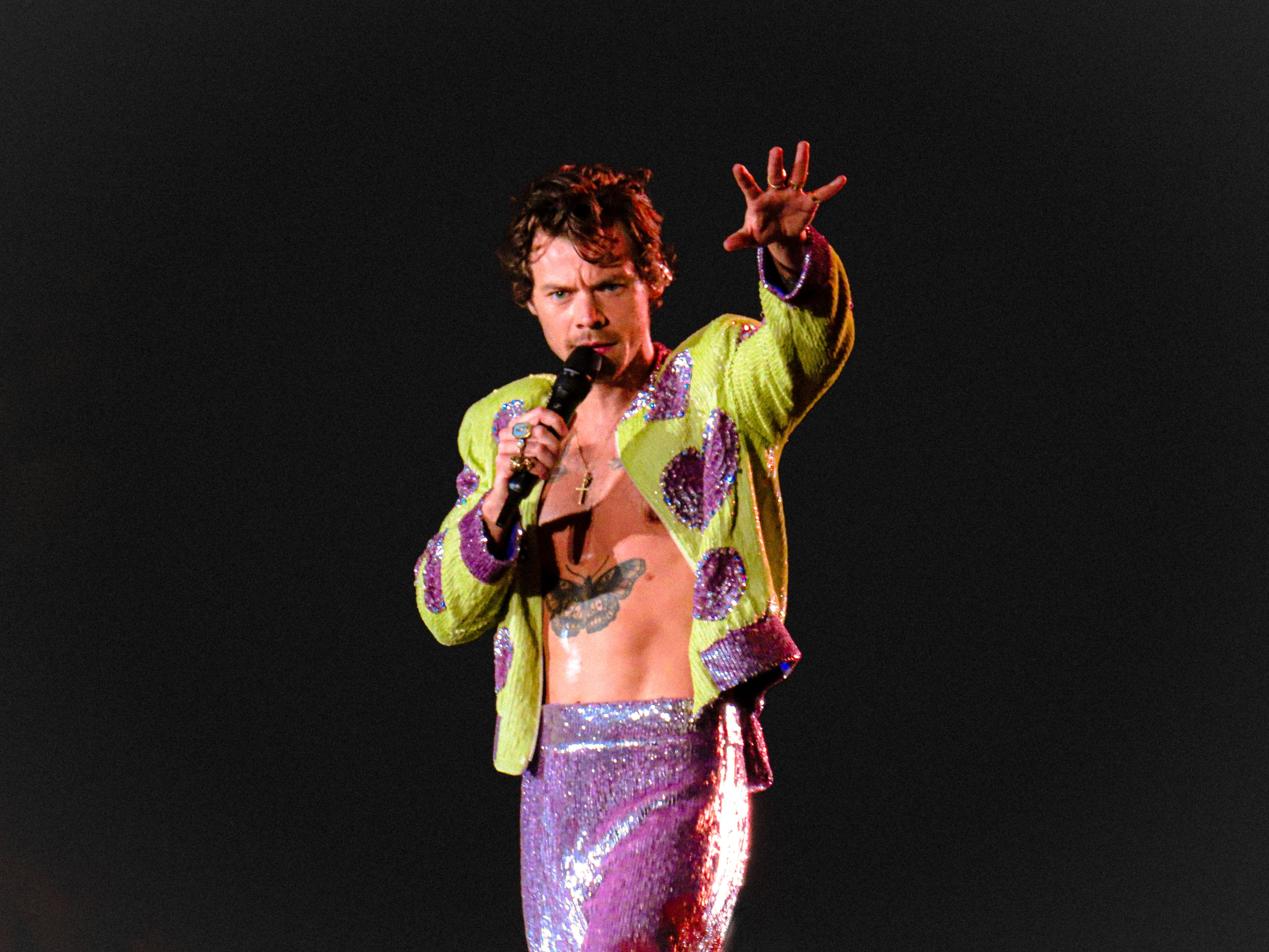 Harry Styles wearing a purple and yellow outfit performing at a concert