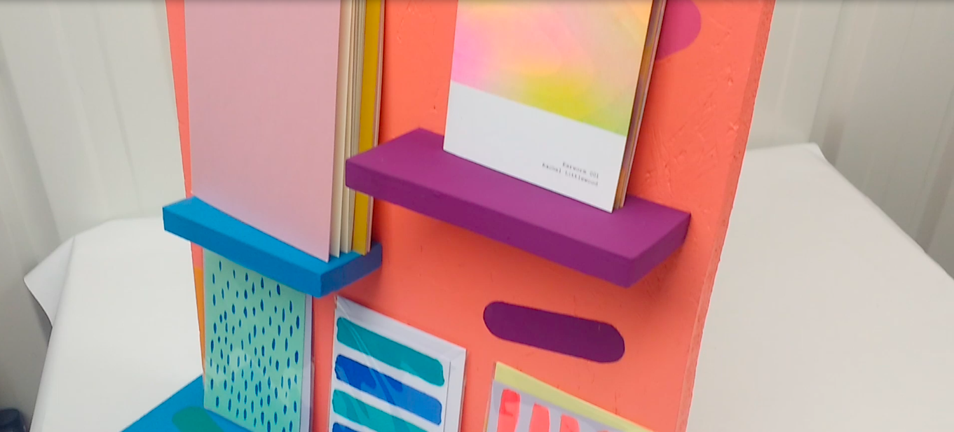 Photograph of shelves constructed from wood, painted in vibrant colours with books and cards resting on the shelves