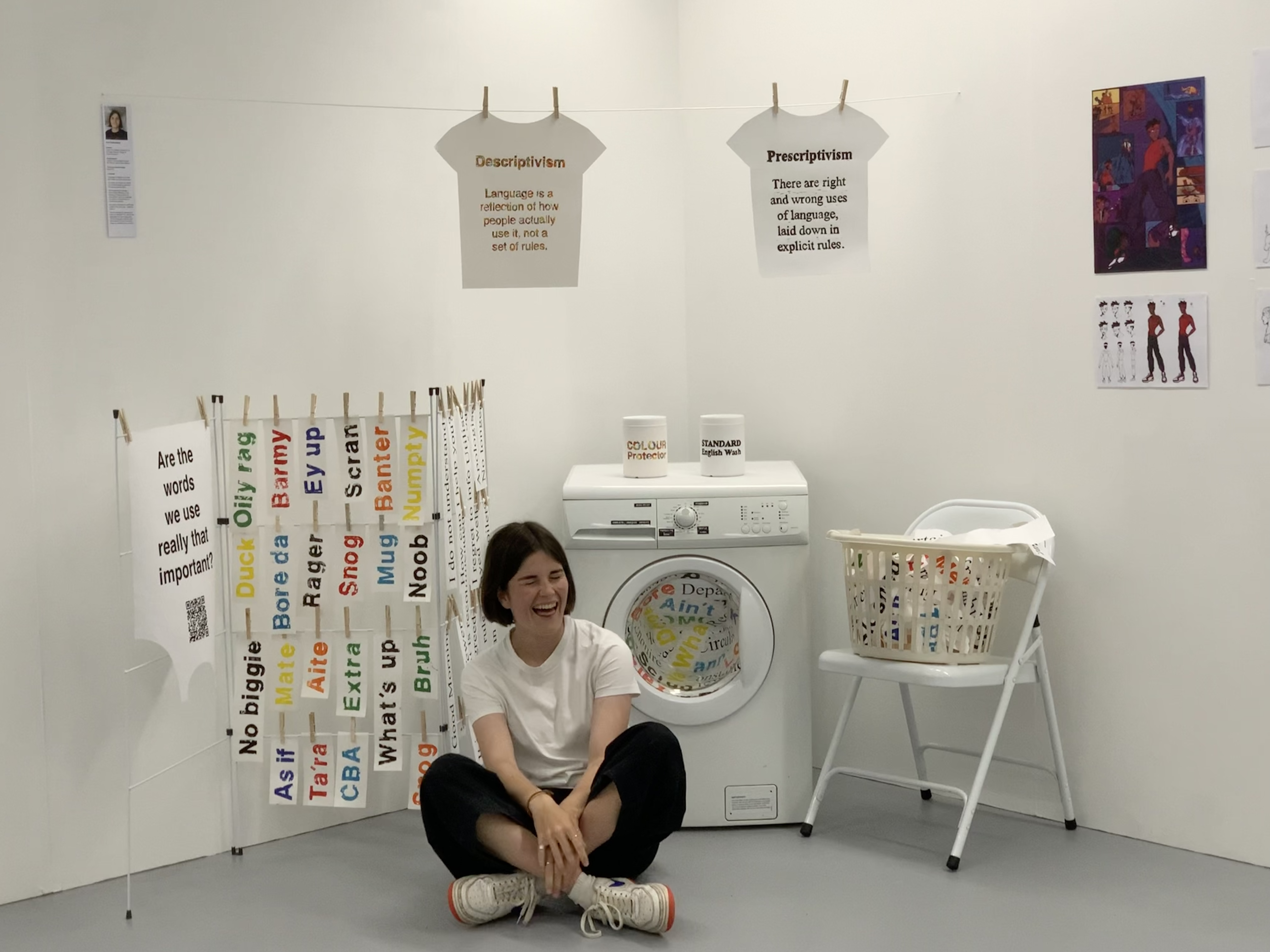 Ava sits cross legged and laughing in the center of frame. Behind her is an artistic display of washing hanging, a washing machine and a washing basket on a chair. Greetings from around the world are written on the laundry in different colours, and the title of the project reads 'Are the words we use really that important?'