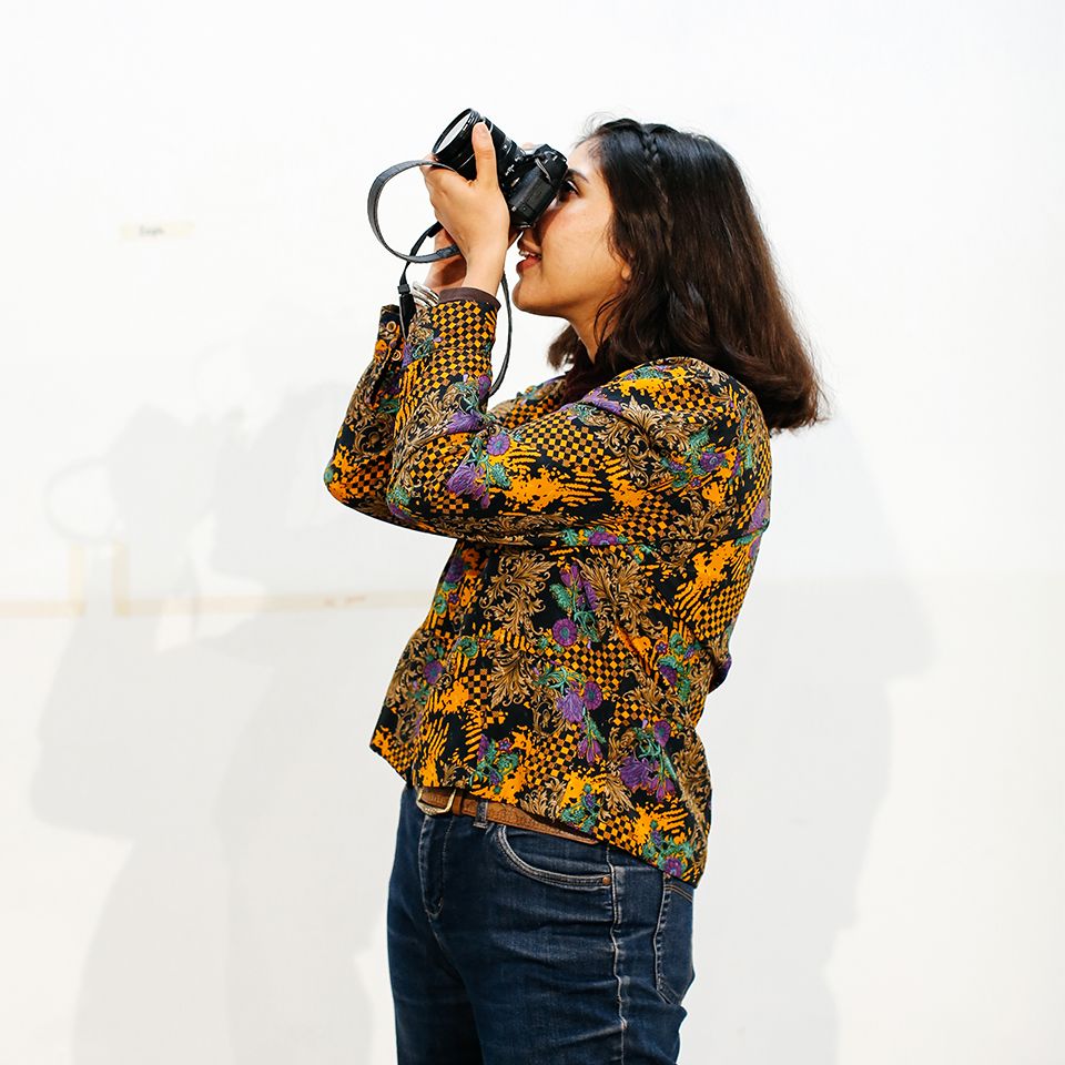 A student holds a camera to their face, looking through the viewfinder and pointing it towards the sky