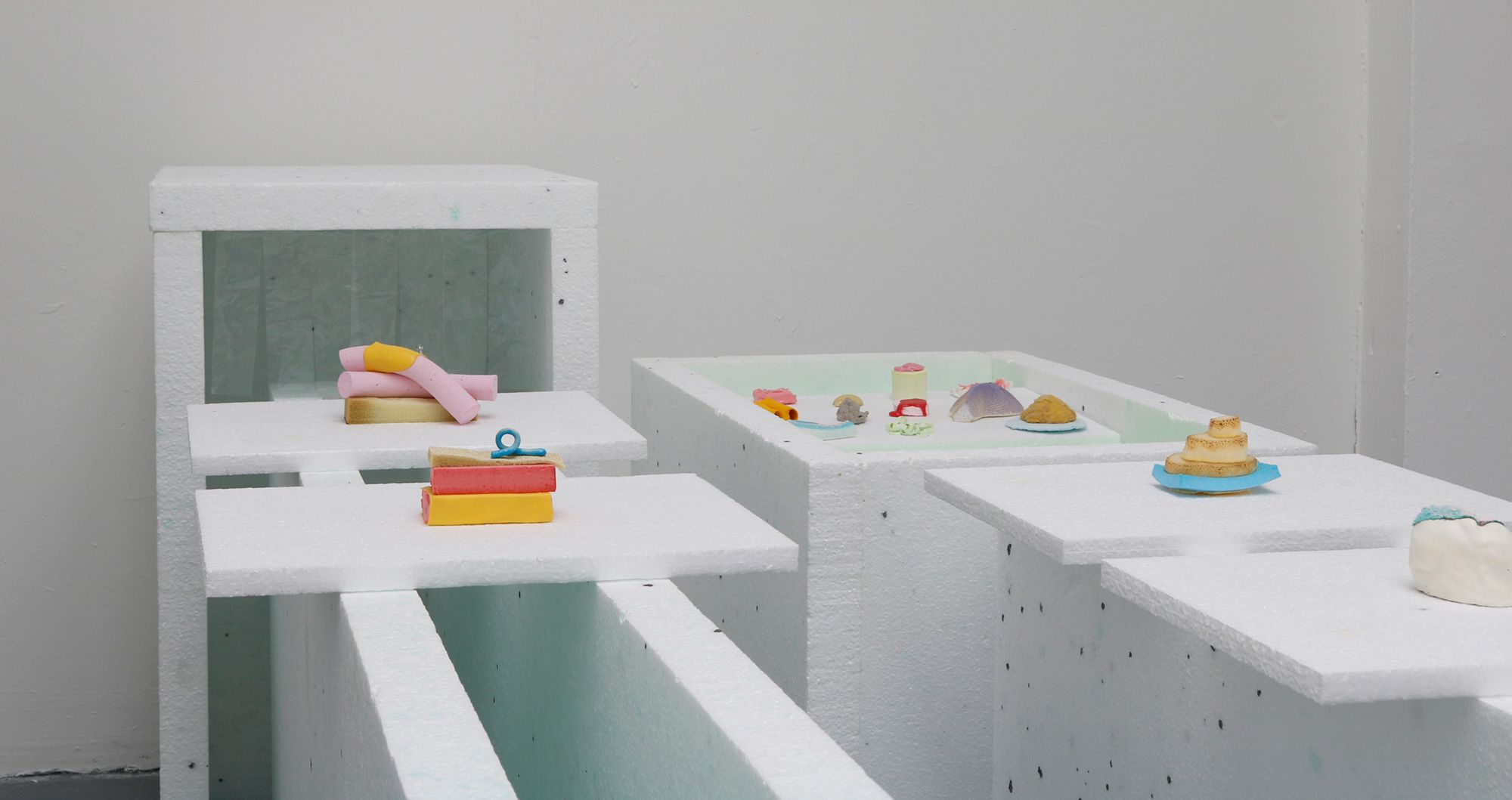 white foam board creates a conveyer belt which holds a series of brightly coloured sculptures created from a range of materials 