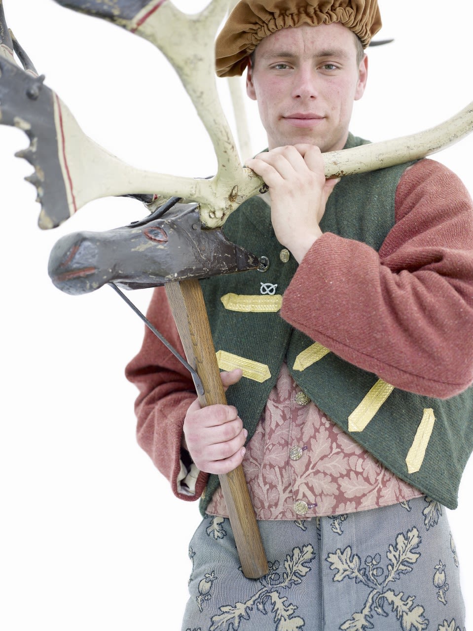man in folk dress holding model on a pole of stag head and antlers