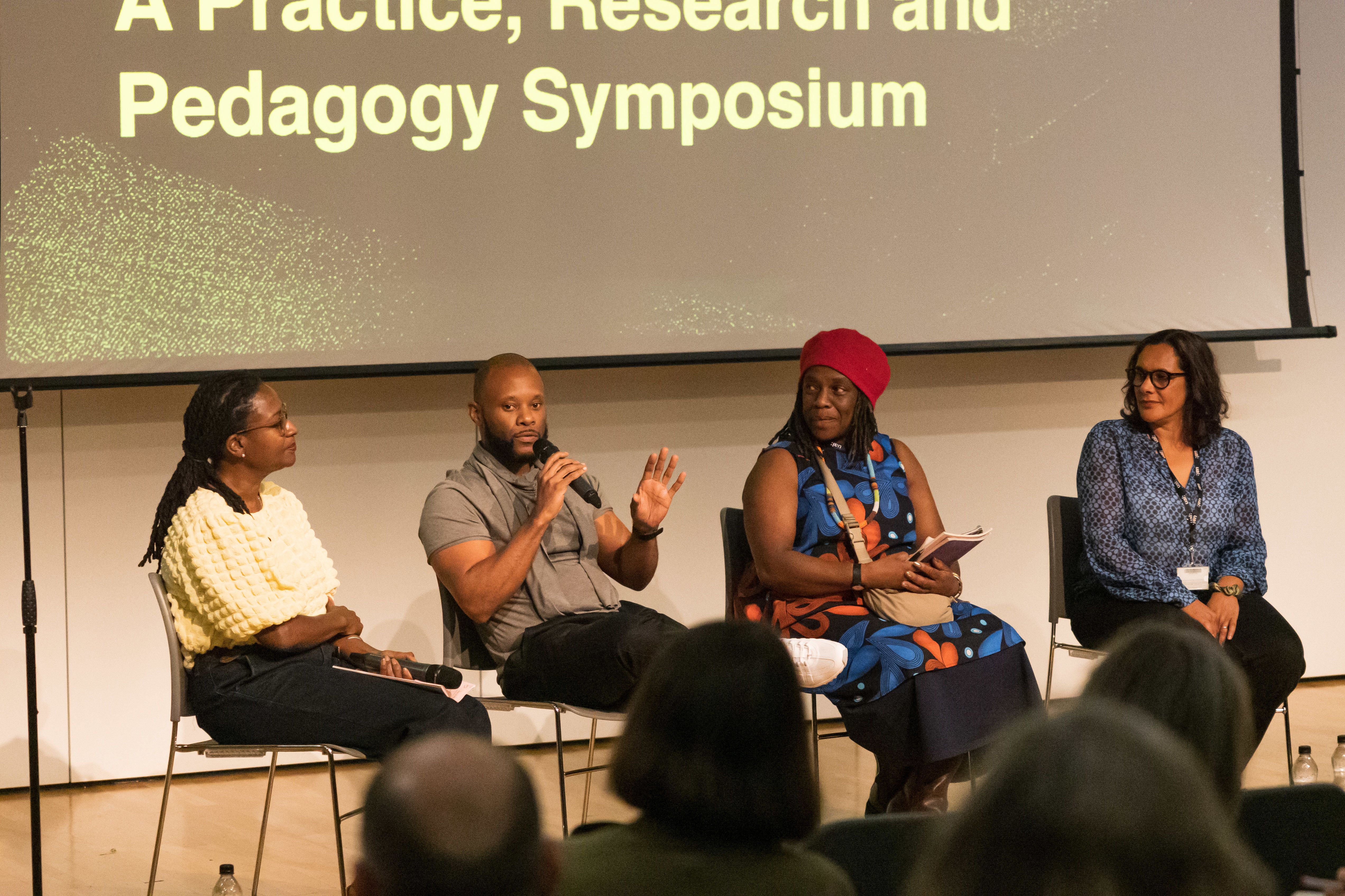 Four speakers sit on panel, at the front of event. 